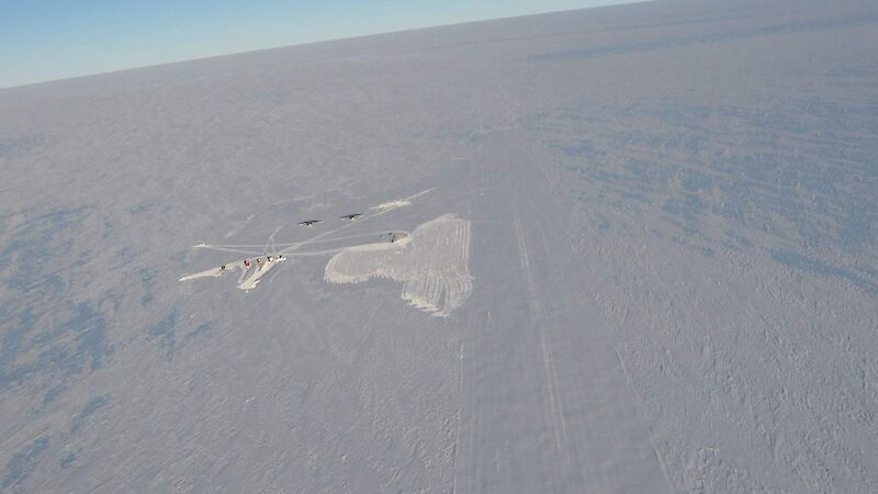 A shot from way up high shows cleared area of snow with some vehicles looking tiny on the ground. This shot shows the curve of the earth at the horizon.