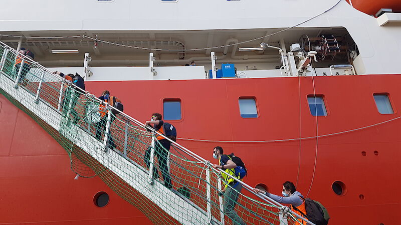 Expeditioners walk up the stairs to a large orange and white ship.