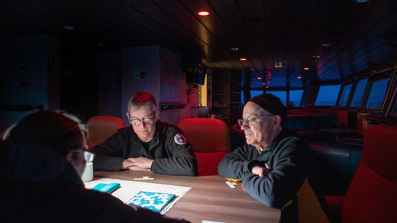 3 crew members sit around a table in the evening on a ship.