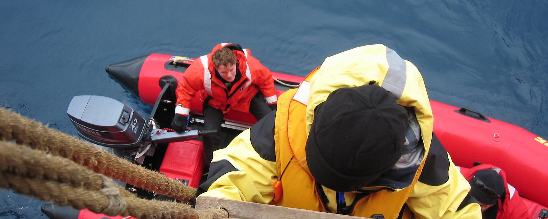 Photo taken from above of someone climbing down a rope ladder into a rubber boat.