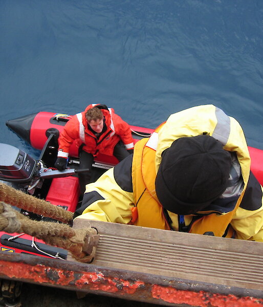 Photo taken from above of someone climbing down a rope ladder into a rubber boat.