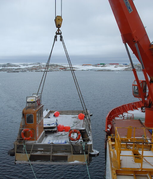 Barge suspended on a cable from a crane over the side of a ship