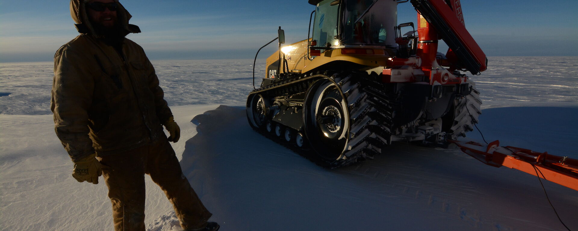 An expeditioner standing next to the Challenger tractor, on the Antarctic tundra