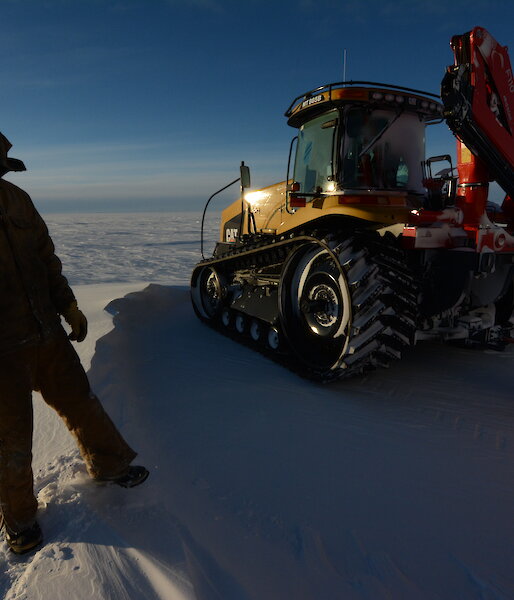An expeditioner standing next to the Challenger tractor, on the Antarctic tundra