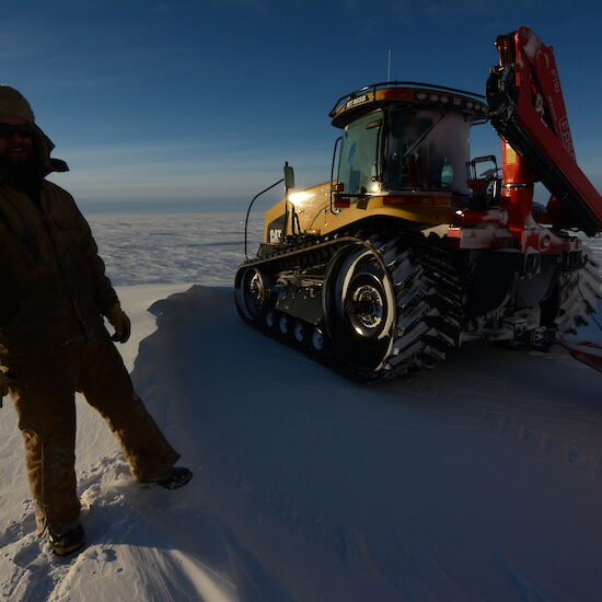 An expeditioner standing next to the Challenger tractor, on the Antarctic tundra