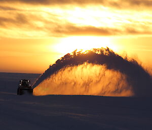 Machinery clearing runway at dusk with snow being projected out like a fountain.