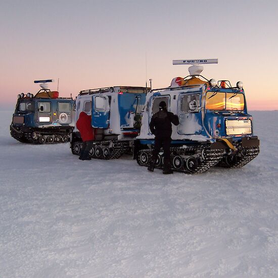 Two vehicles park in the snow with men emerging from each vehicle
