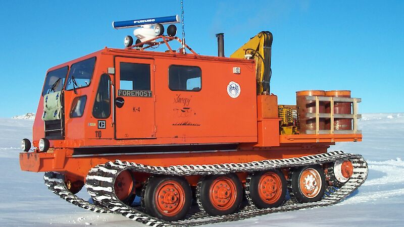 Orange vehicle with a cab for passengers and tracks.