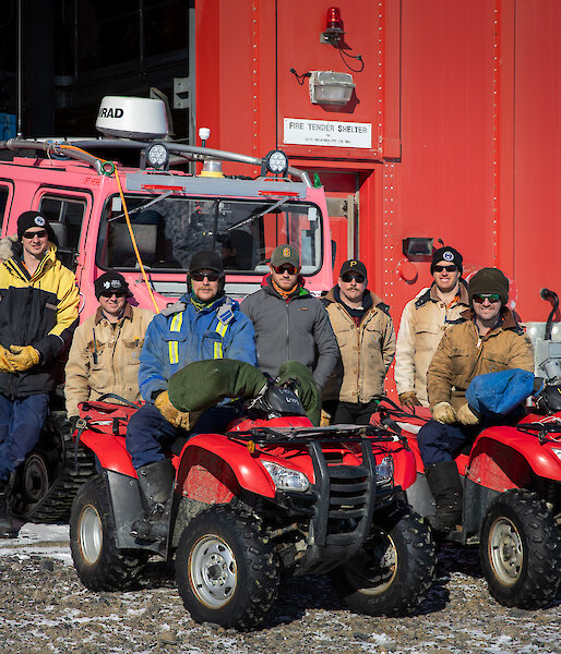 Group of expeditioners outside workshop standing near quads