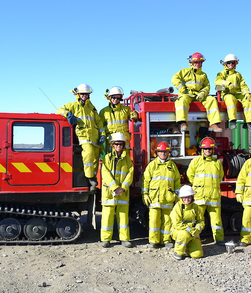 Expeditioners in fire fighting gear pose near and on the fire Hägglunds.