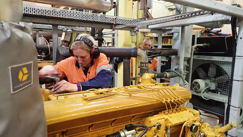 A female mechanic works on a large generator inside the power house at Davis station