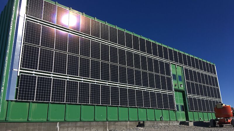 A wall of solar panels, mounted on a green building.
