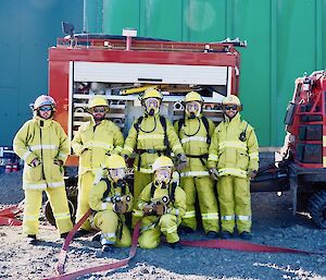 Group of expeditioners in fire fighting clothing standing around the oversnow vehicle