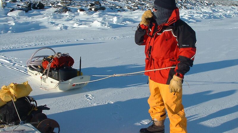 Expeditioner in cold weather gear speaks into a hand-held radio