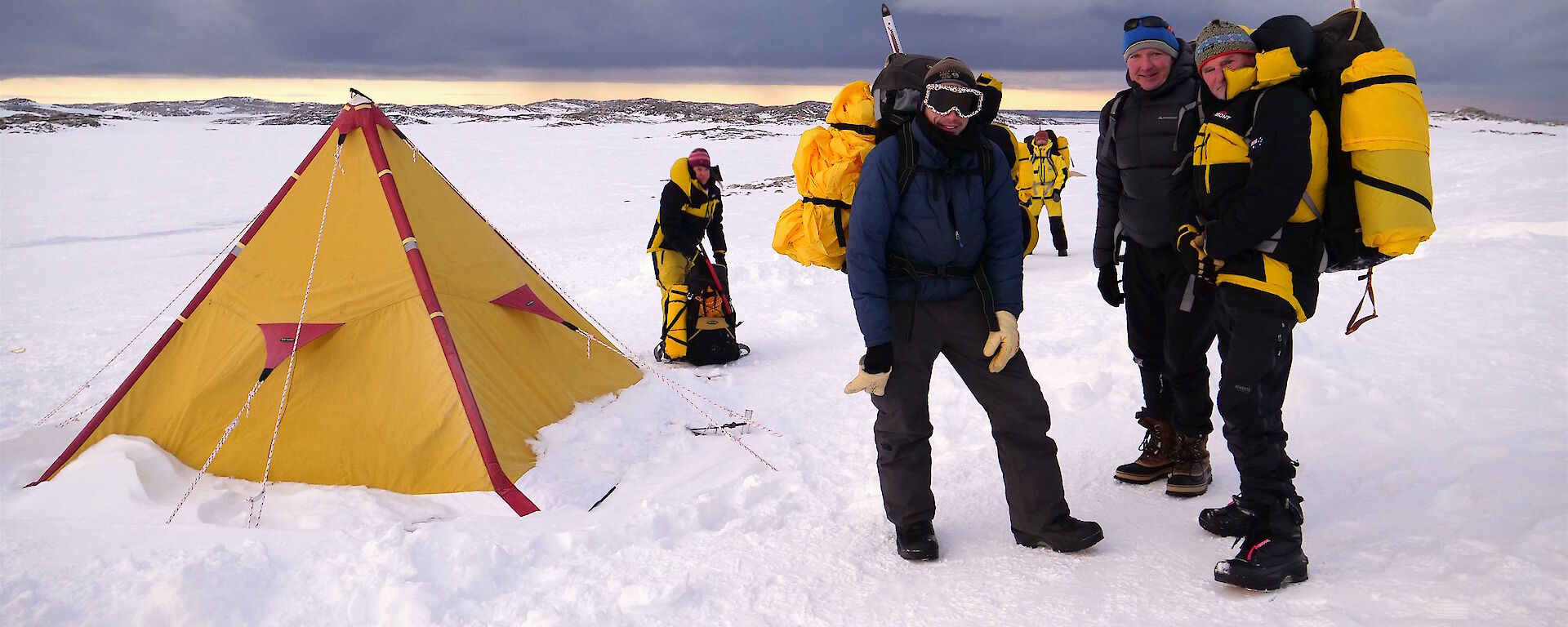 Expeditioners with backpacks standing near tent