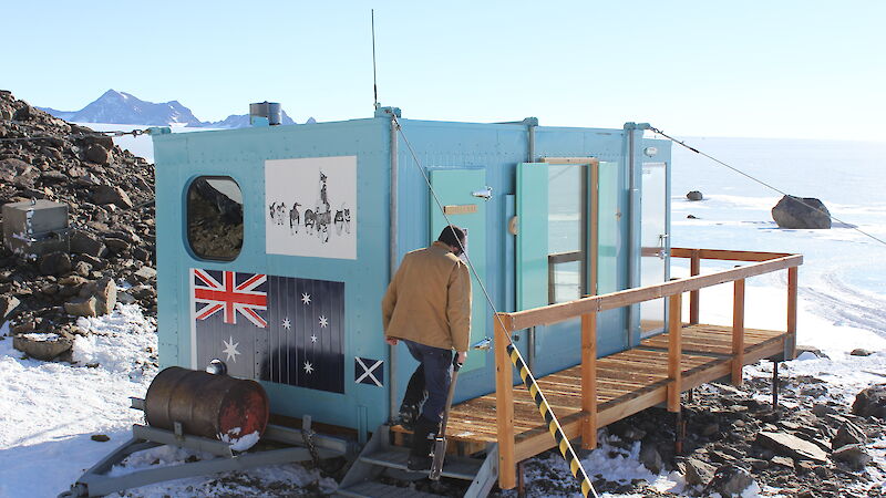 Expeditioner climbing stairs of small field hut