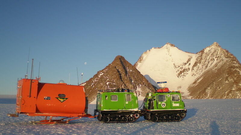 Red van on skis being pulled by a Hagglund.