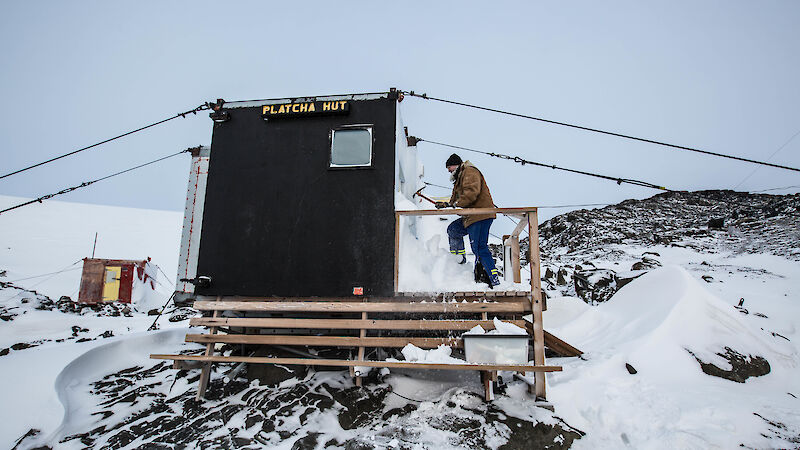 Expeditioner using pick to remove ice from outside small hut