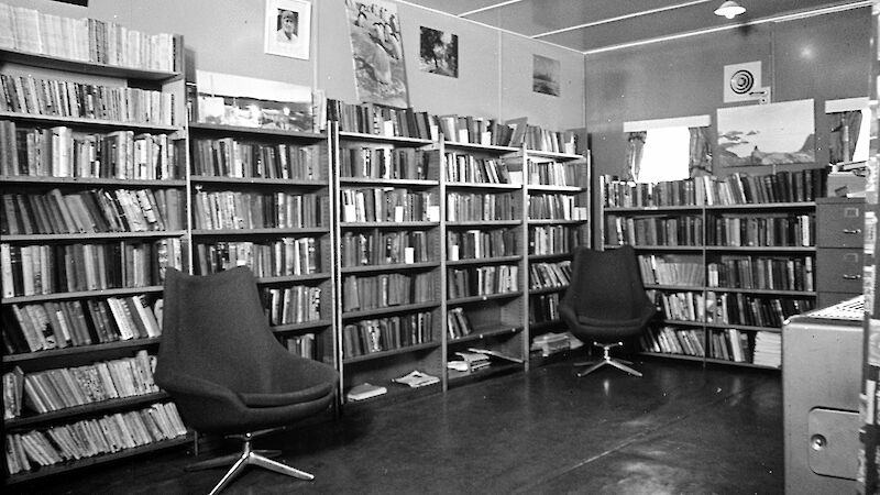 Black and white image of interior of library with book shelves against walls.