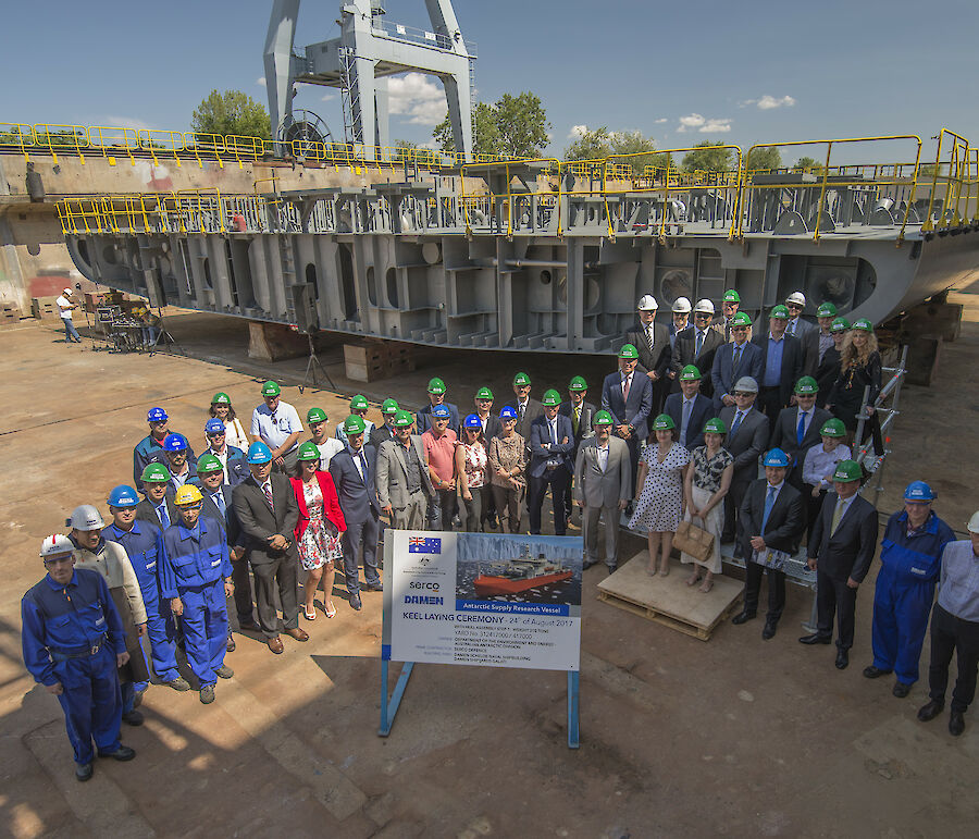 Looking down at line up of workers and AAD delegation in front of hull section at keel laying ceremony for new icebreaker