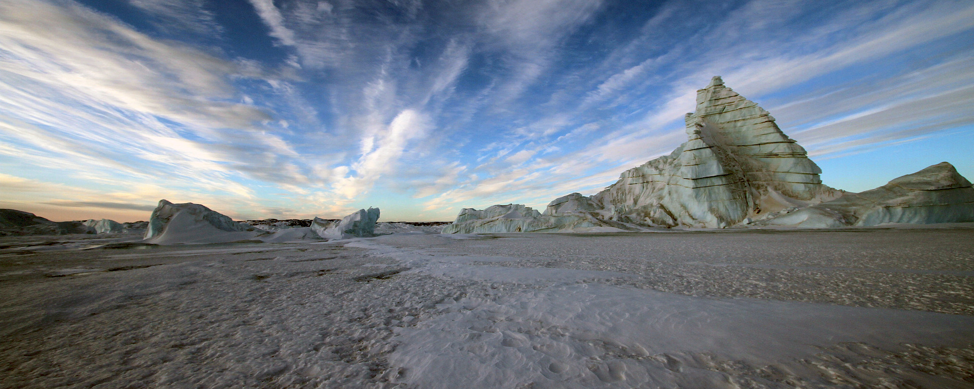 Grounded icebergs sourned by fast ice and wind streaked clouds above