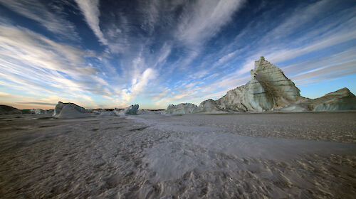 Grounded icebergs sourned by fast ice and wind streaked clouds above