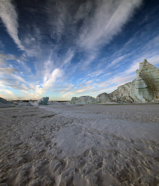 Grounded icebergs sourned by fast ice and wind streaked clouds above