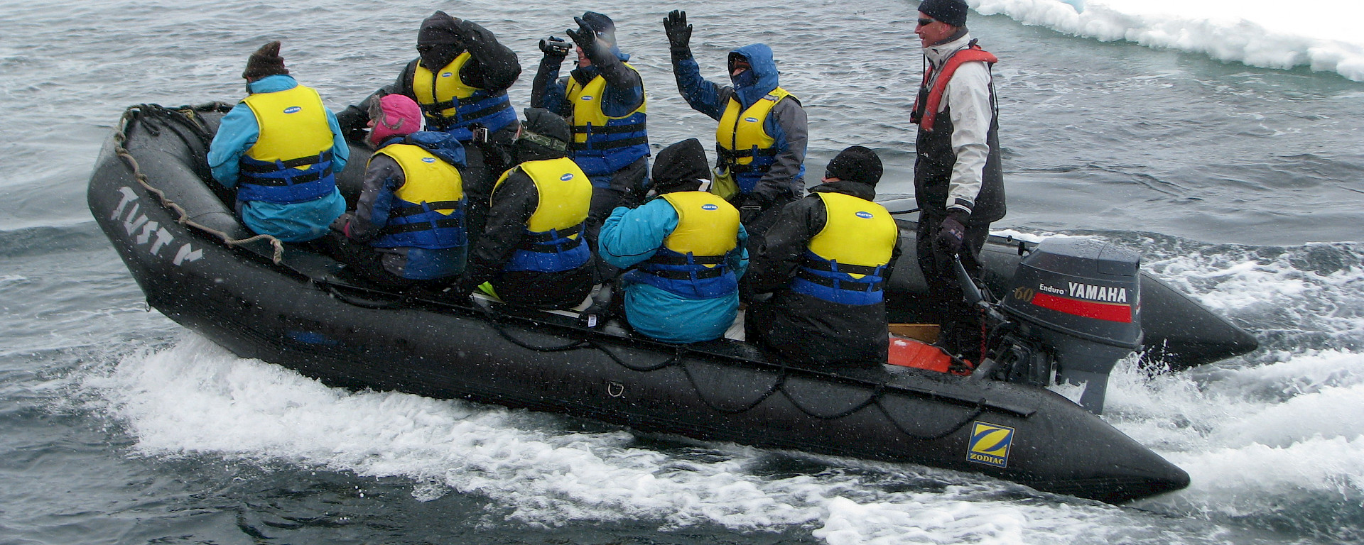 Eight tourists in an inflatable rubber boat, with an ice floe in the background