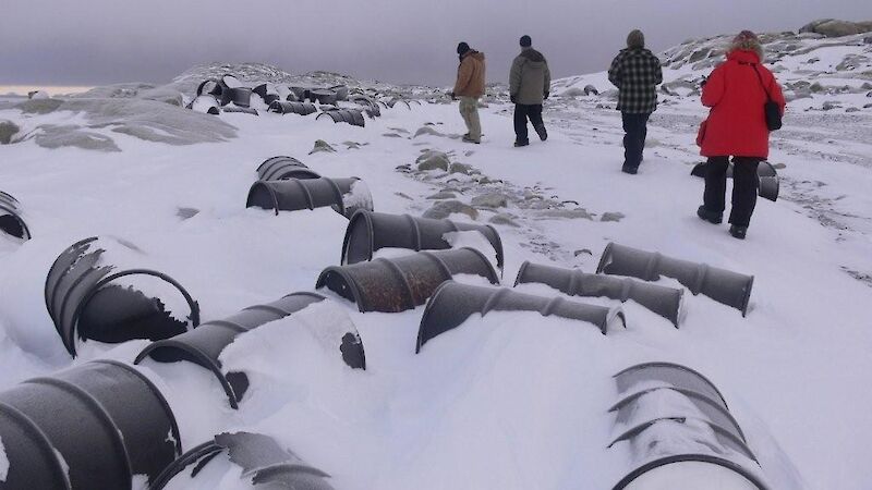 Fuel drums mostly covered with snow. People in the background.