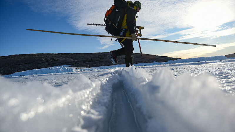Expeditioner with an ice drill walking on the sea ice