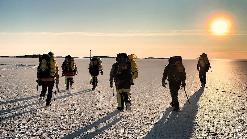 Group of expeditioners walking on the ice towards the sun at the horizon