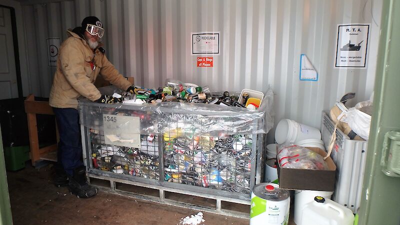 An expeditioner stands next to a cage of bottles and cans.