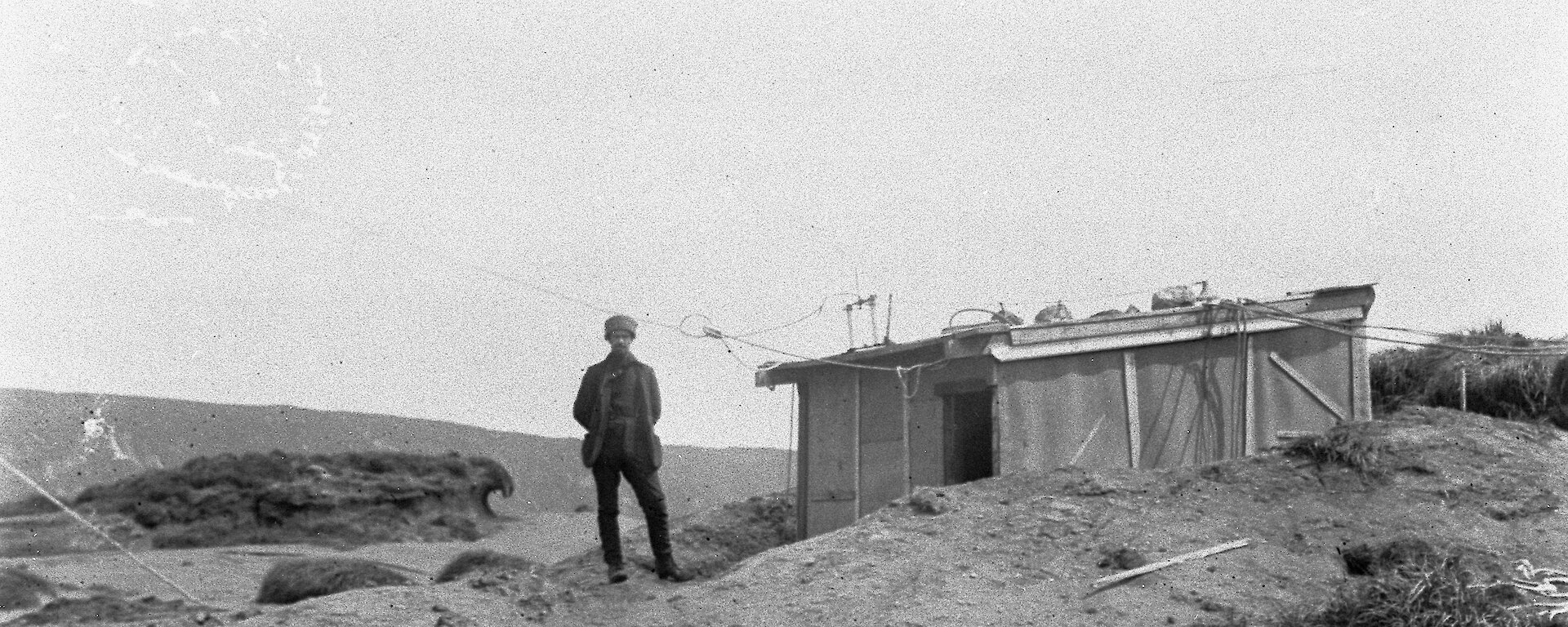 Black and white photo of a person standing at the door of a simple hut.