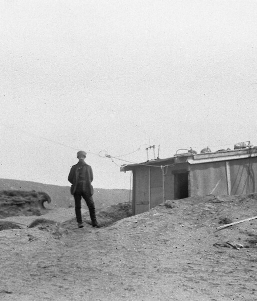 Black and white photo of a person standing at the door of a simple hut.