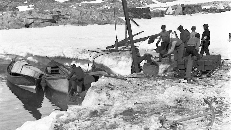 Boats with equipment and frame of air tractor alongside small ice cliff