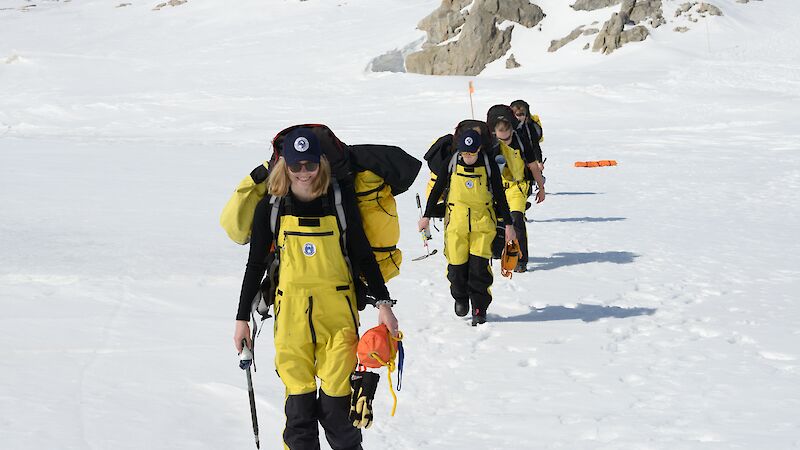 Expeditioners walk through a snow-covered landscape.