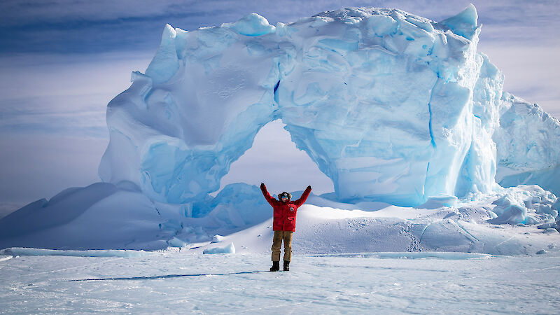 Smiling expeditioner standing in front of a glacier with arms raised up