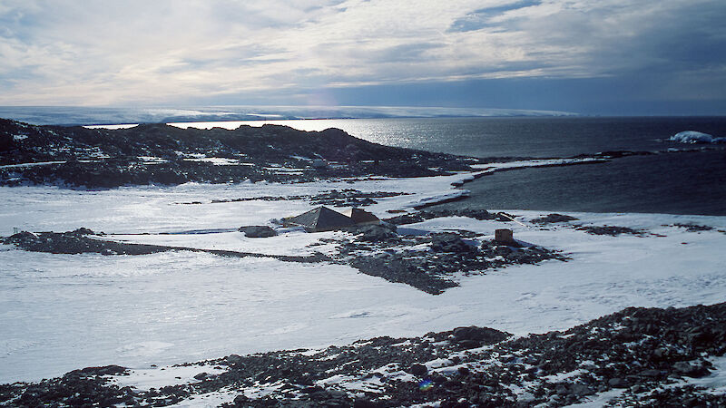 Aerial shot showing the bay, the peninsula and the wooden hit that looks very small compared to the sea and icy landscape.