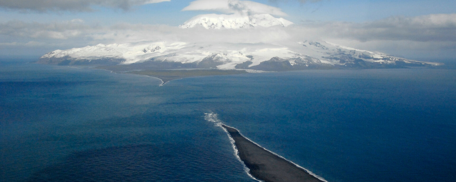 A photo from the air of a small island in the foreground and the snowy topped Big Ben on Heard Island in the background.