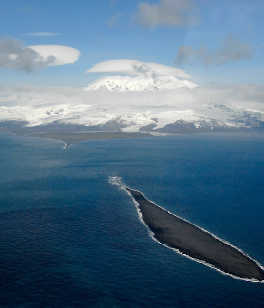 A photo from the air of a small island in the foreground and the snowy topped Big Ben on Heard Island in the background.