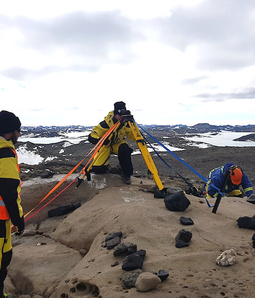 3 people with surveying equipment in a rocky landscape.