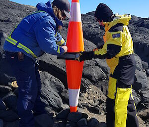 Two people placing large witches hats in a rocky landscape