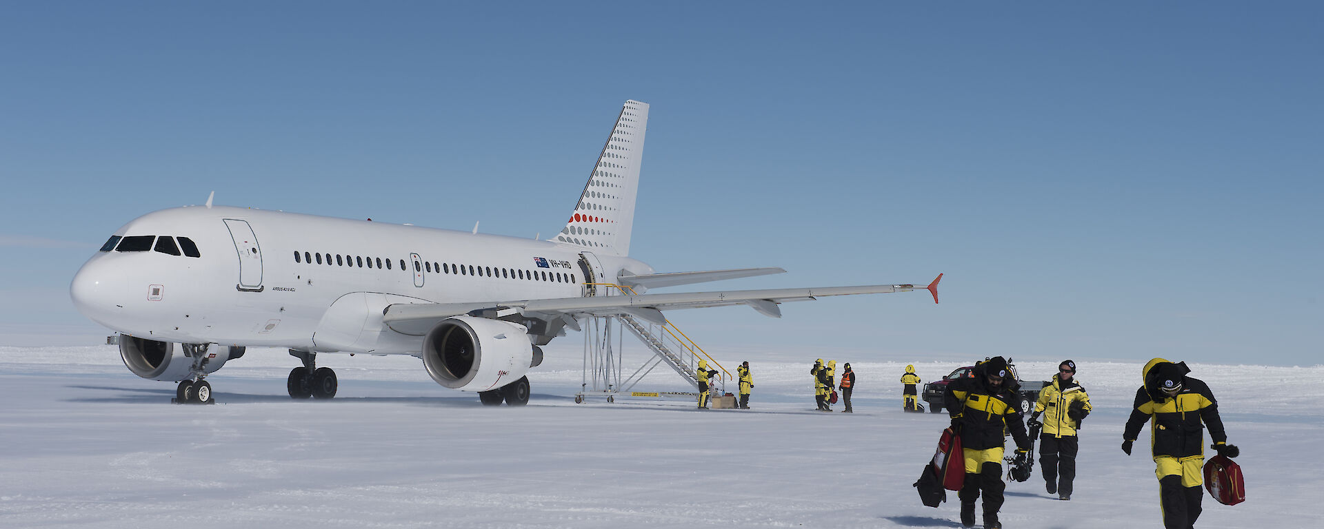 A photo of people walking off a icy runway with a plane in the background