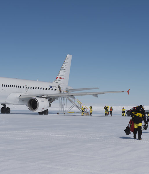 A photo of people walking off a icy runway with a plane in the background