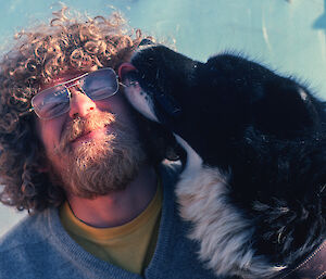 Tom Maggs with his face being licked by a husky