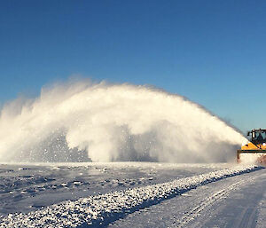 A tractor blowing an arc of snow