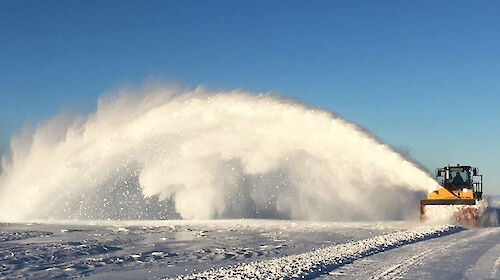 A tractor blowing an arc of snow