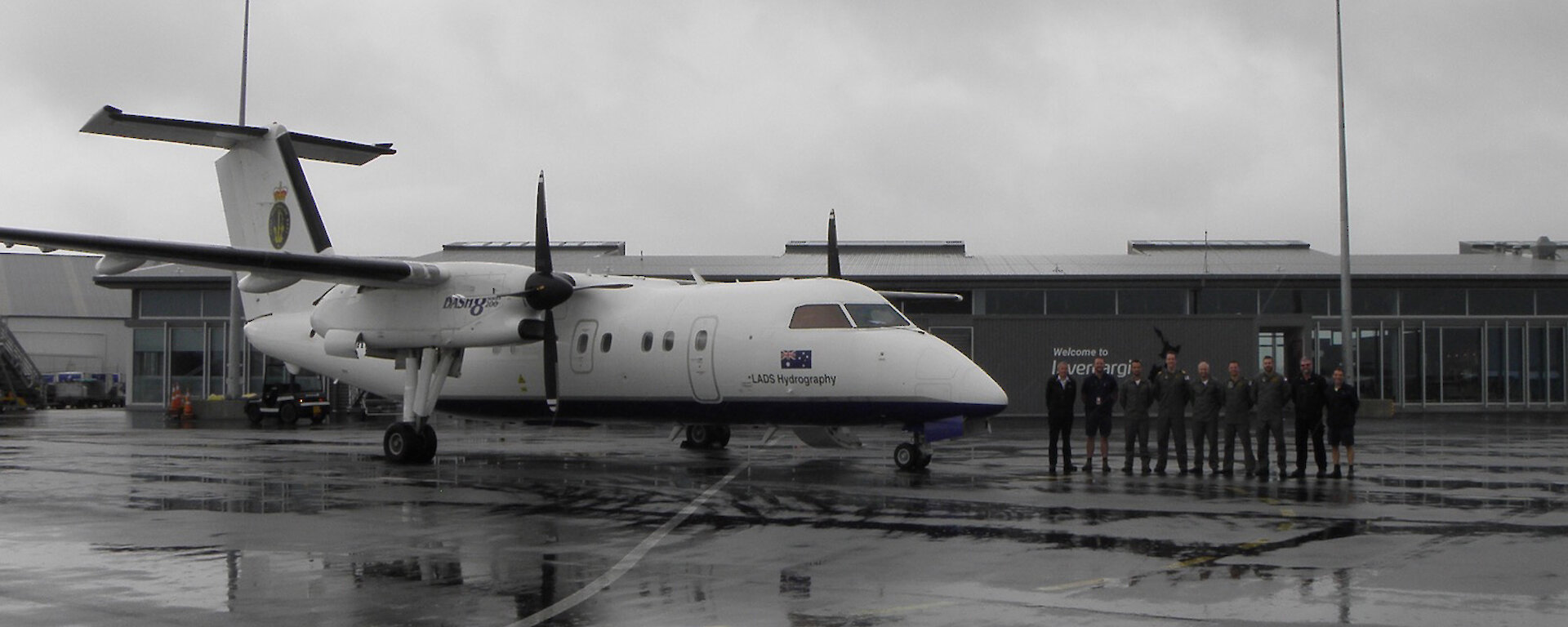 The Dash 8 on the runway at Invercargill with the nine person survey team standing beside.
