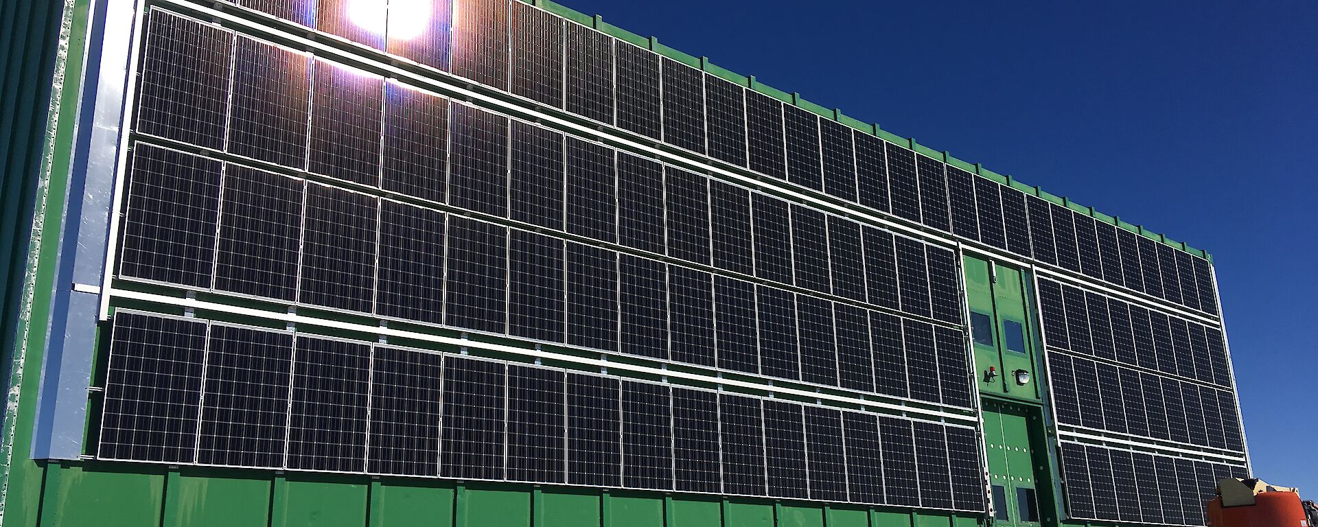 The 105 solar panel array installed, with a wind deflector visible down the length of the array on the left side of the building, to minimise the effects of high wind speeds during blizzards.