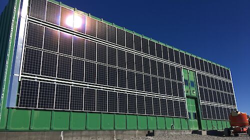 The 105 solar panel array installed, with a wind deflector visible down the length of the array on the left side of the building, to minimise the effects of high wind speeds during blizzards.